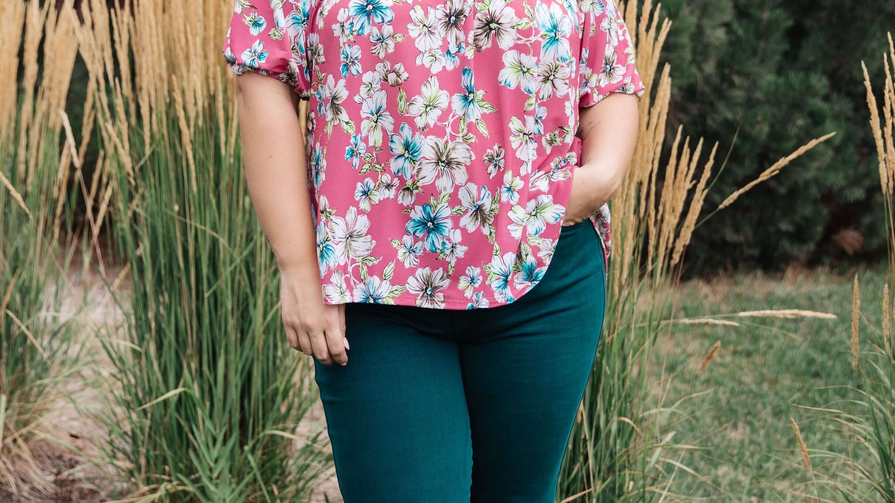 Woman wearing floral top and green jeans in nature, demonstrating fashionable jeans that embrace every curve for a perfect fit.