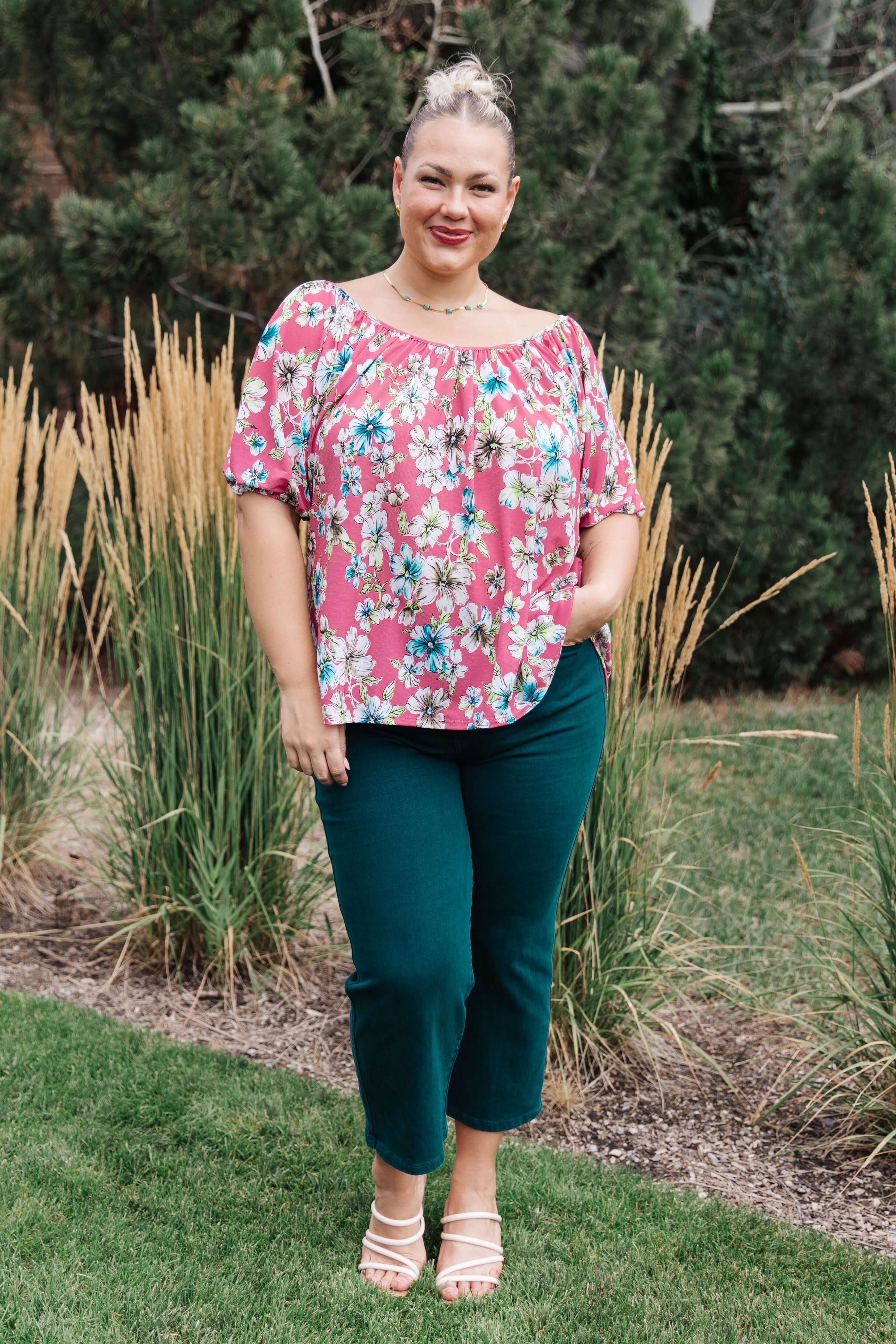 Woman wearing floral top and green jeans in nature, demonstrating fashionable jeans that embrace every curve for a perfect fit.