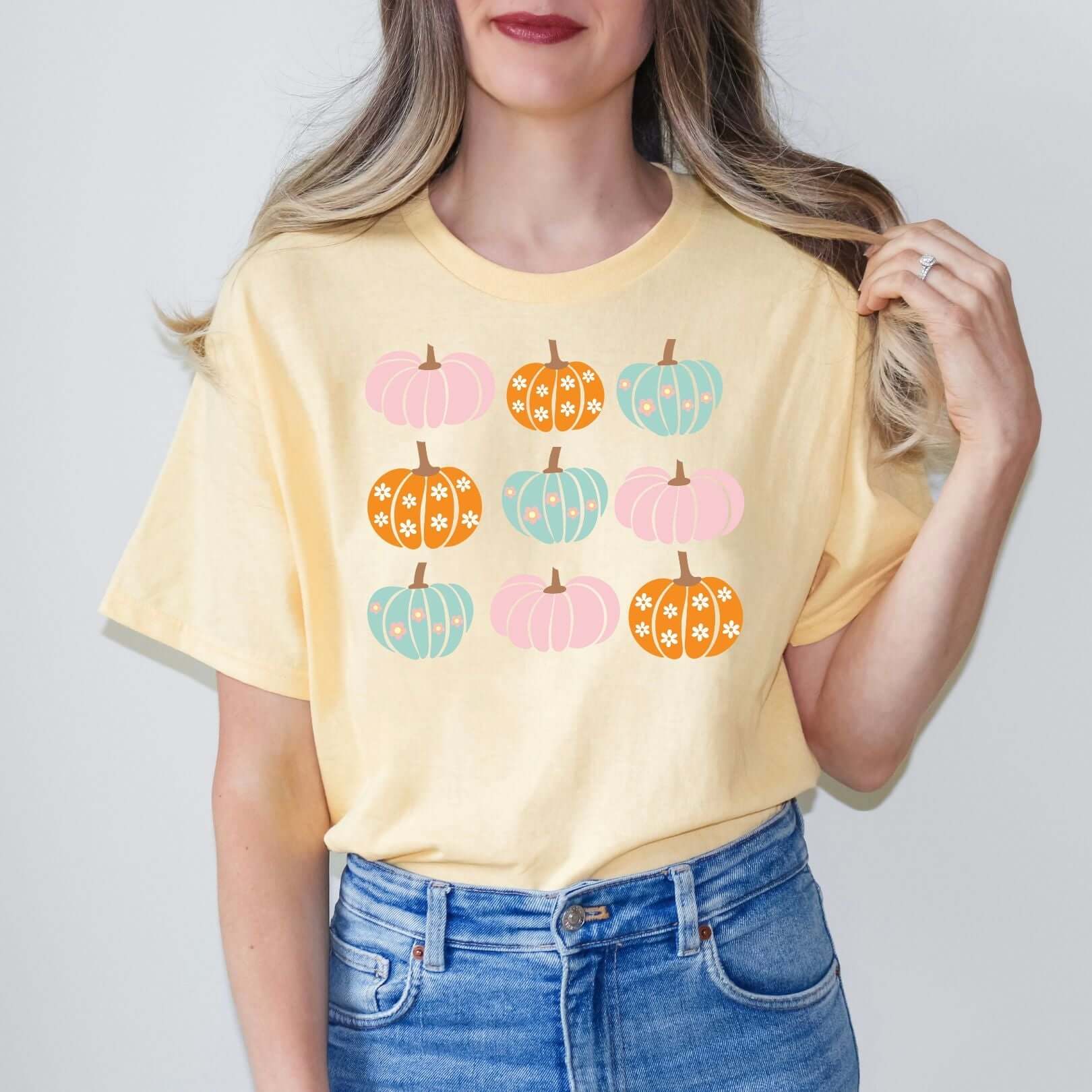 Woman wearing a light yellow Cheerful Pumpkin Graphic Tee from SugarGlowCo with colorful pumpkin designs, made of 100% cotton for a relaxed fit.