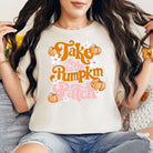 Woman wearing Take Me to the Pumpkin Patch Graphic Tee in cream color with multicolor DTF printing, sitting on a couch.