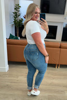 Woman wearing Nicole Tummy Control Skinny Jeans in vintage wash, turning to look in a mirror, showcasing the fit and style of the jeans.