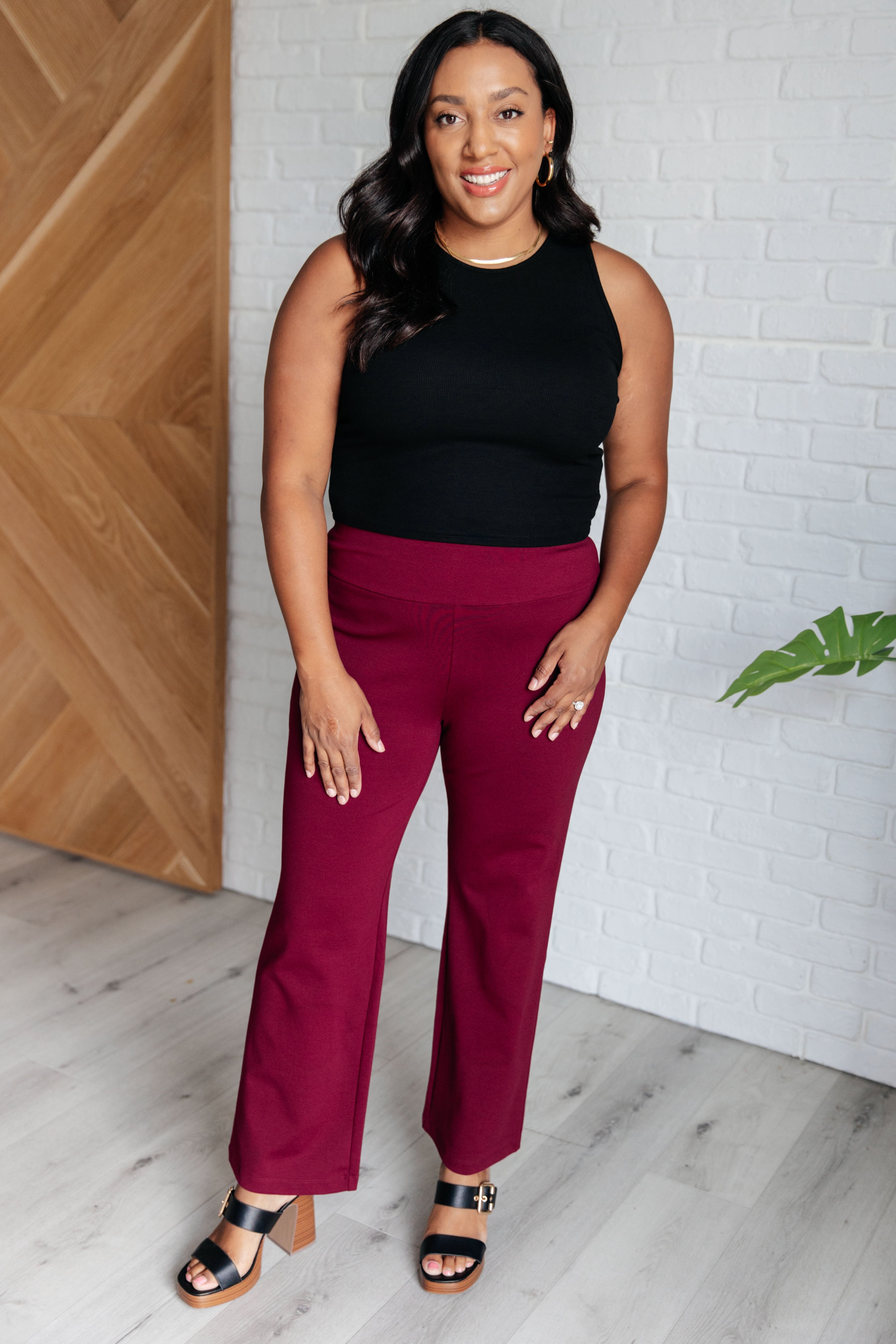 Woman wearing Magic Straight Pants in Wine with black top and heels standing indoors.