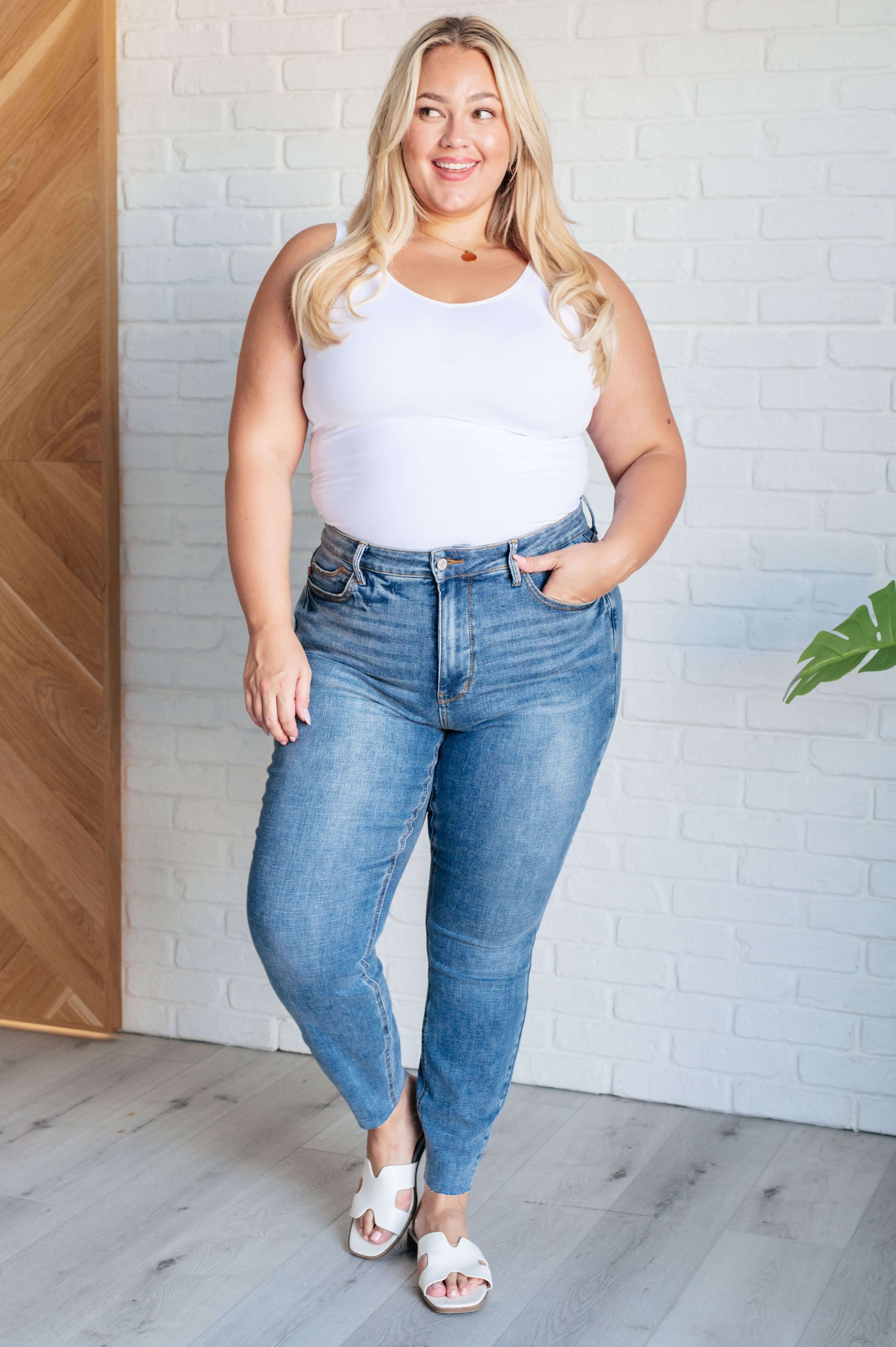 Woman wearing Nicole Tummy Control Skinny Jeans in vintage wash standing against a white brick wall by Judy Blue.